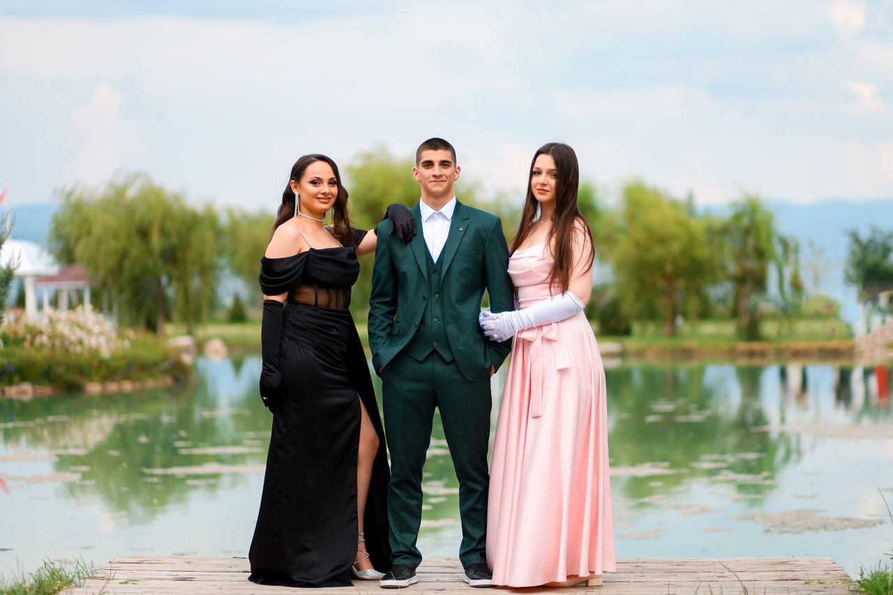 Three elegantly dressed adults posing by a beautiful lakeside with a serene background.