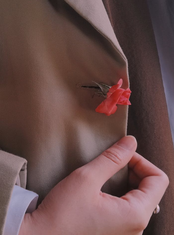 Mastering the First Impression: Your intriguing post title goes here A close-up of a hand adjusting a rose boutonniere on a suit jacket, reflecting elegance and style.